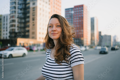 Young woman smiling, looking away with hope and confidence, standing on a city street at golden hour, portraying modern urban life and future aspirations