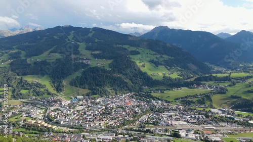 Aerial drone view of Planai mountain and the town of Schladming in the Austrian Alps. Summer sunlight illuminates the alpine landscape while dark storm clouds gather over the mountains