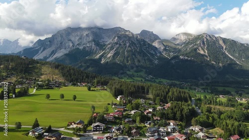 Aerial drone view of the Dachstein mountain near Ramsau am Dachstein in Austria. Slow flight over green alpine meadows, traditional mountain houses and forests in warm summer sunset light.