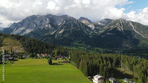 Aerial drone view of the Dachstein mountain near Ramsau am Dachstein in Austria. Slow flight over green alpine meadows, traditional mountain houses and forests in summer sunset light.