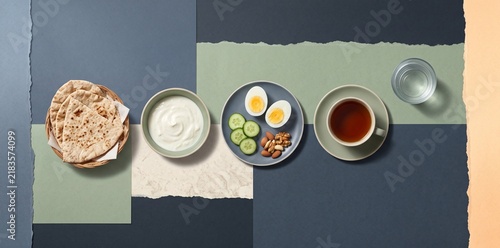 Top-view Ramadan Suhoor meal with flatbread, eggs, yogurt, cucumber, nuts, tea and water arranged across layered matte paper in a calm pre-dawn food collage