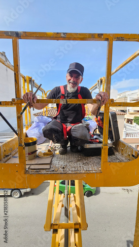 Real senior professional painter aged 63–66 working on a residential building from an elevated platform
