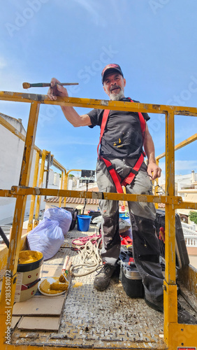 Real senior professional painter aged 63–66 working on a residential building from an elevated platform