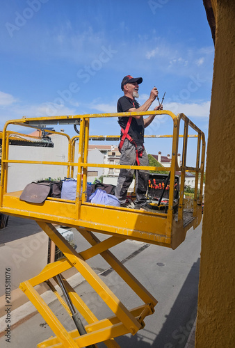 Real senior professional painter aged 63–66 working on a residential building from an elevated platform