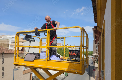 Real senior professional painter aged 63–66 working on a residential building from an elevated platform
