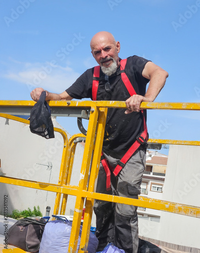 Real senior professional painter aged 63–66 working on a residential building from an elevated platform