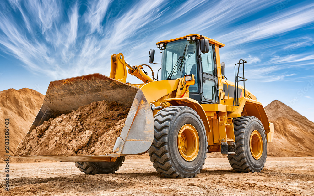 Fototapeta premium Yellow wheel loader scooping earth at construction site