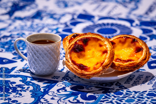 Three pastel de nata custard tarts with coffee cup on blue tablecloth