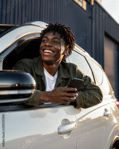 Smiling driver leaning out of car window holding phone