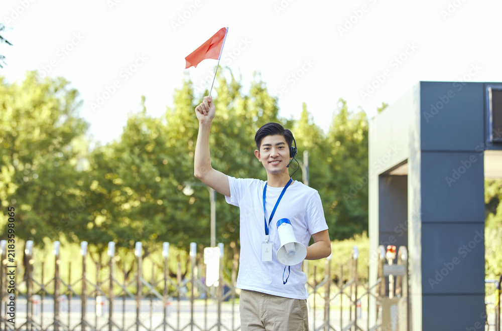 Fototapeta premium Young male tour guide with red flag and megaphone outdoors