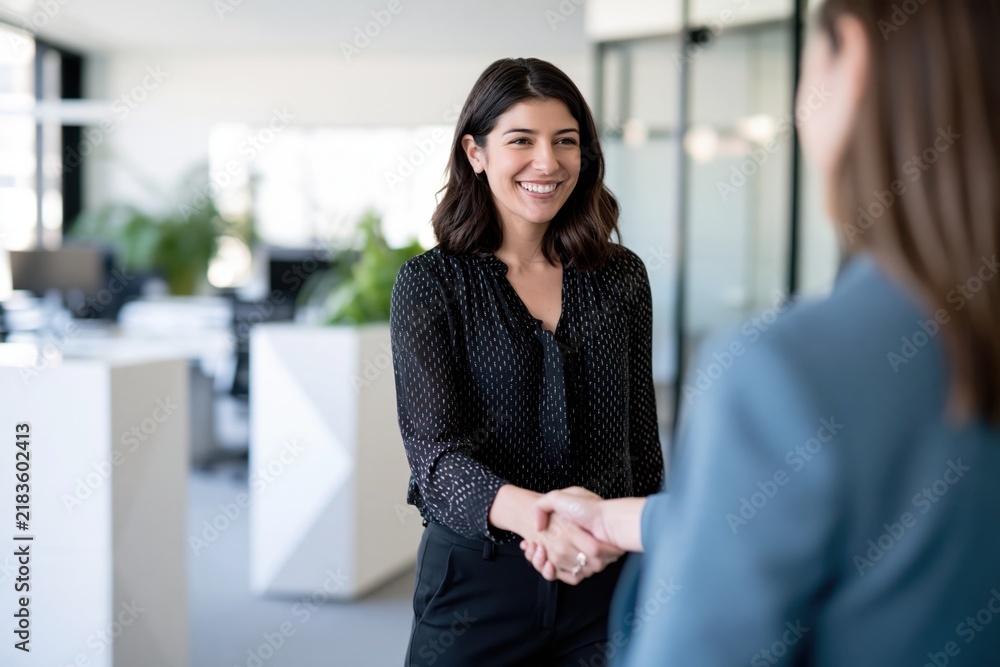 Obraz premium Smiling businesswoman shaking hands during meeting in modern office, confident female manager or executive greeting client, making agreement and successful business deal