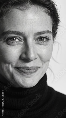 Vertical video: Pulling back camera woman in turtleneck shifting to smile in soft light for warmth