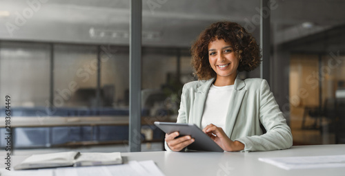 Canvastavla Smiling latina business woman coordinator sitting at desk, using digital tablet beside paper documents