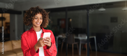 Canvastavla Young Latin woman using smartphone phone, texting with smile in modern office lounge