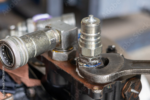 Photography Steel wrench tightening quick disconnect hydraulic coupler onto machinery manifold inside repair workshop