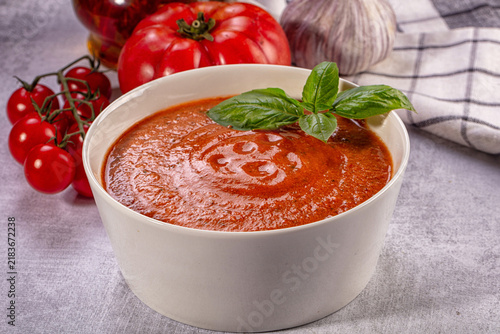 Foto Bowl of fresh gazpacho soup garnished with basil leaves, surrounded by ripe toma