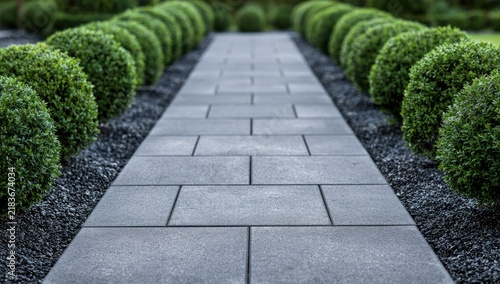 A straight, stone-paved garden path lined with perfectly manicured boxwood shrubs