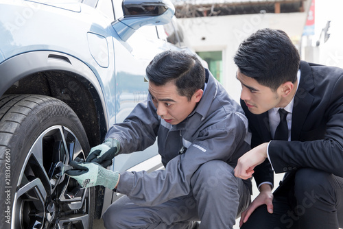 Fotografía Mechanic repairing tire on electric car while suited observer watches