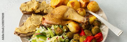 Konstfotografi A plate holds baked chicken leg, potatoes, fresh salad, roasted Brussels sprouts, and chickpea bread