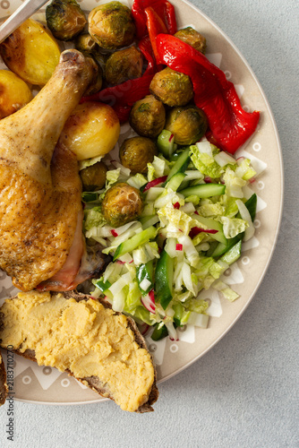 Cuadro en lienzo A plate holds baked chicken leg, potatoes, fresh salad, roasted Brussels sprouts, and chickpea bread