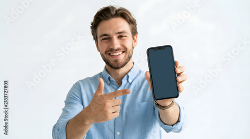 Smiling man pointing at blank smartphone screen for mobile app advertisement mockup