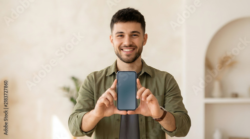 Smiling man showing blank smartphone screen to camera for mobile app advertising mockup.