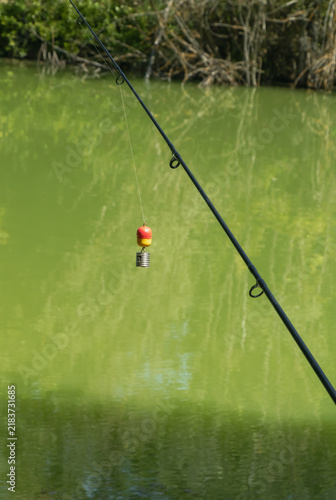 фотографія Fishing rod with float and feeder hanging above calm green pond water in quiet f