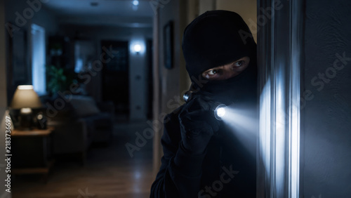 Masked intruder using a flashlight inside a dark home, burglary in progress, property crime plus household security risk