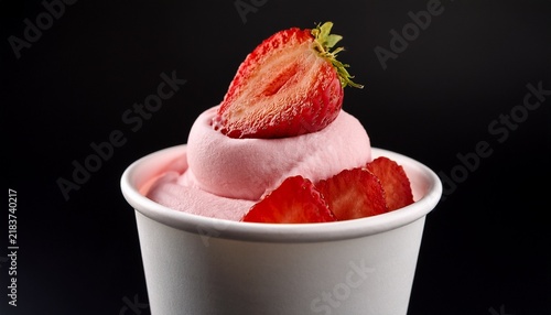 strawberry frozen yogurt in a white cup with strawberry slices on top against a black background