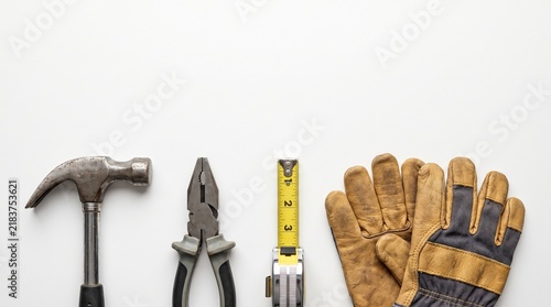 Assorted construction tools and leather gloves arranged on a clean white background for repair.