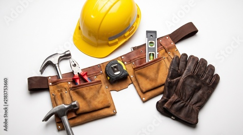 Yellow hard hat and leather tool belt arranged for professional construction site maintenance.