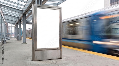 Blank vertical billboard mockup standing on a modern train station platform for advertising.