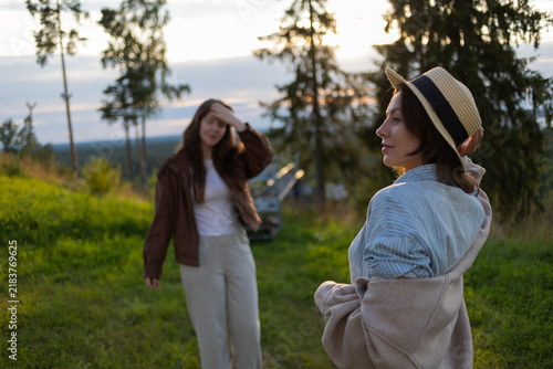 Evening walk of two young women on a hilltop, sun flare through the branches of spruces