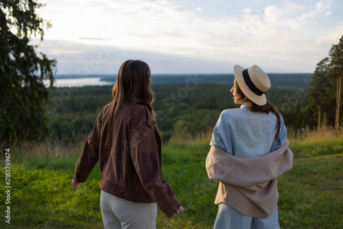 Back view of two friends walking side by side above a wide forest at sunset