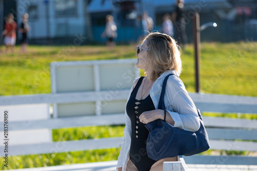 Woman with a beach bag walking to the water, summer day at a lakeside recreation park.