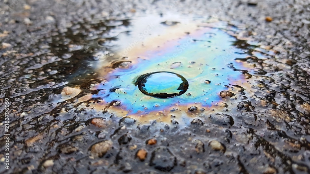 Obraz premium Oil slick puddle with rainbow sheen on wet asphalt representing pollution environmental contamination and urban water runoff