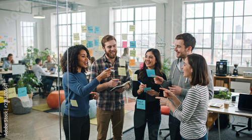 Diverse professional team brainstorming with sticky notes on glass wall in modern office