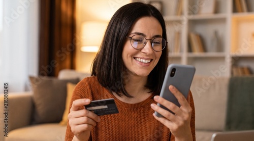 Smiling woman with glasses holding a credit card and looking at her smartphone with an online shopping confirmation on screen, suggesting a successful purchase