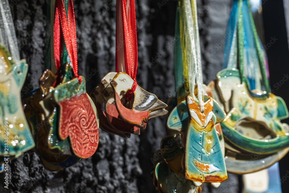 Fototapeta premium Colorful handmade ceramic Christmas ornaments, birds, mittens, foxes and angels hang from satin ribbons on a dark display backdrop, creating a festive, artisanal, seasonal and gift-shopping mood