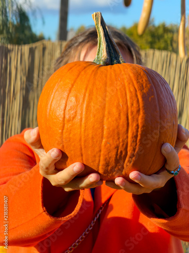 Middle-aged woman holding large orange pumpkin at outdoor autumn market smiling, with woman, holding, pumpkin, autumn detail, showing market, stall, smiling, coat context