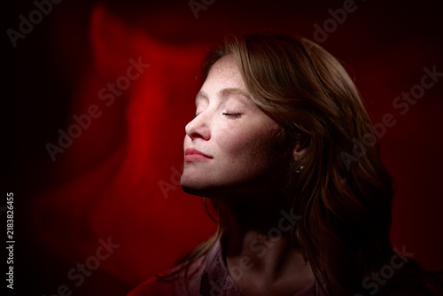 A serene portrait of a woman with eyes closed, illuminated by dramatic red studio lighting and soft shadows, conveying calm, introspection, beauty and a contemplative, cinematic mood.
