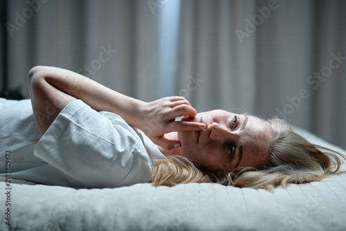Фотография A thoughtful young woman lies on a bed, lost in reflection with her fingertip to her lip