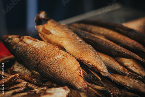 Freshly smoked fish displayed in a market setting, showcasing various sizes and textures of the fish with a blurred background of additional seafood products