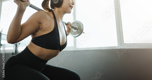 Obraz na płótnie A squat under a barbell turns training into strength for the athlete by tall windows, while another squat keeps the barbell level as training builds strength for the athlete wearing large audio gear