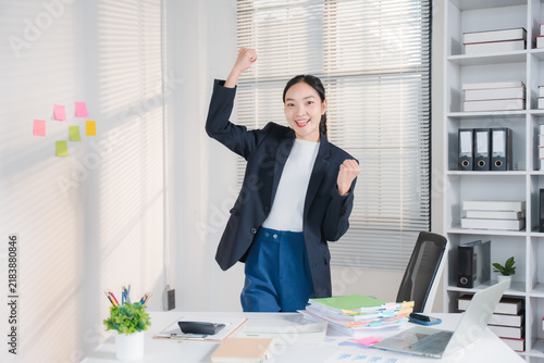 Bild auf Leinwand Excited businesswoman celebrating success in office: A young Asian businesswoman in a dark blazer and blue pants is excitedly celebrating