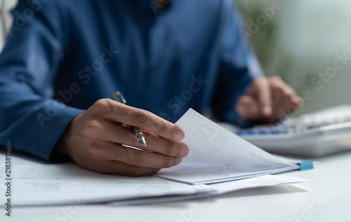 Businessman reviewing financial documents and using calculator at office desk represents accounting, expense analysis, budgeting, tax preparation and professional financial management.