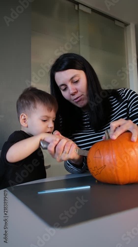 Child cutting pumpkin with mother