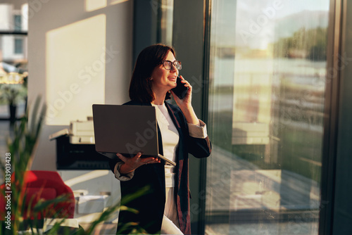 Businesswoman talking on the phone while holding a laptop