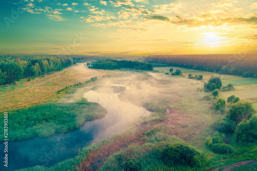 Aerial view of countryside and river in early misty morning. Trees along river. The time before sunrise. View from above