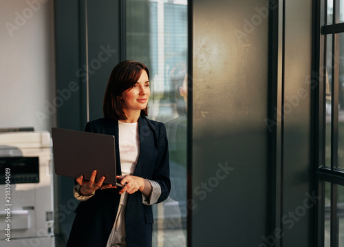 Businesswoman with a laptop looking out an office window